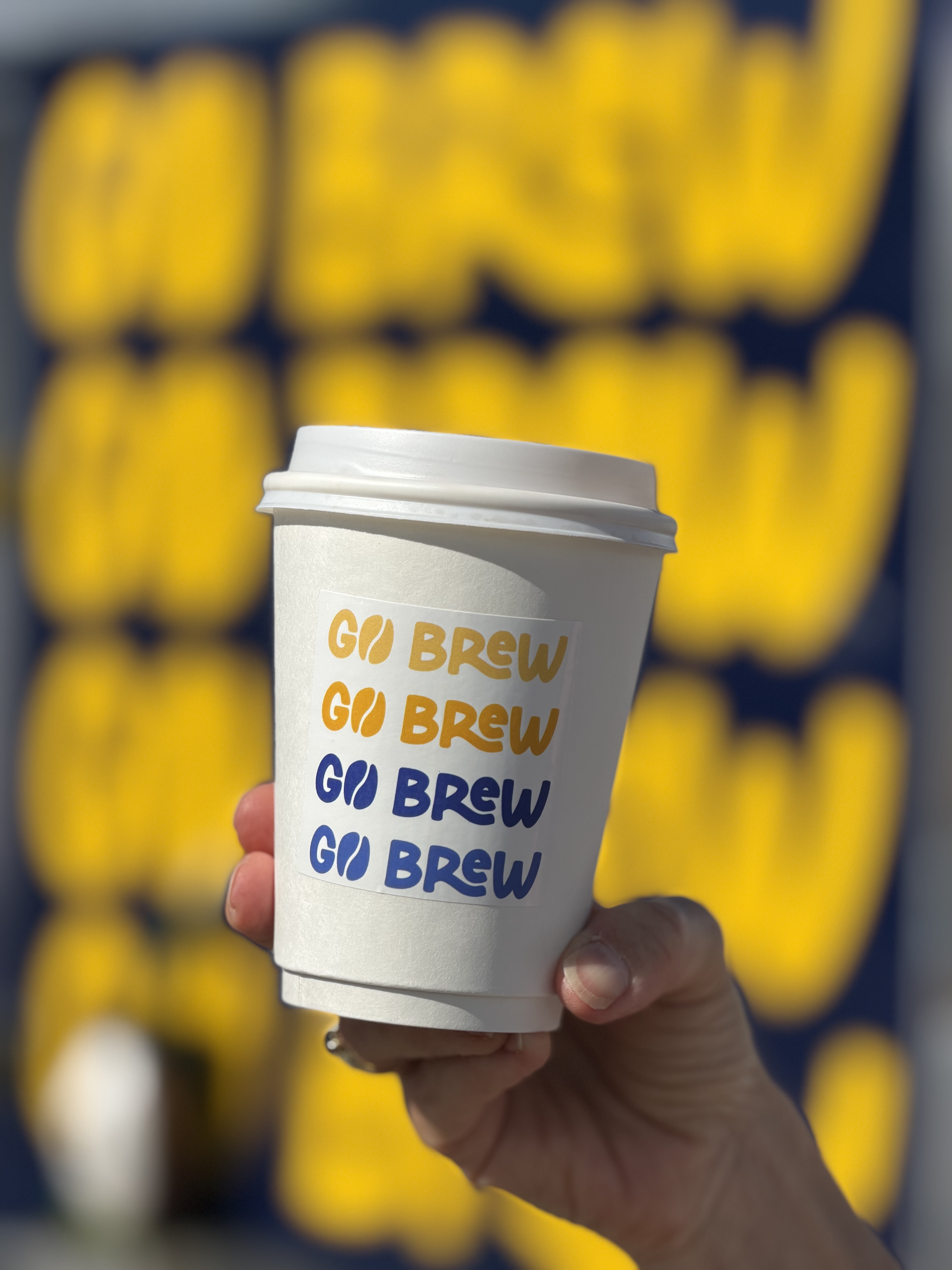 Go Brew hot coffee cup held in front of a yellow Go Brew sign